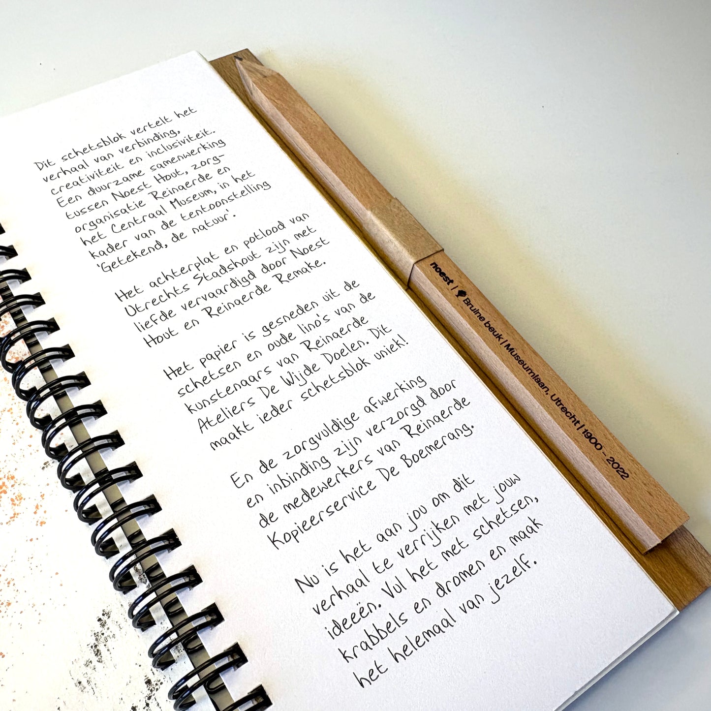 Het schetsblok opengeklapt op tafel, toont gerecycled papier en gepersonaliseerd potlood