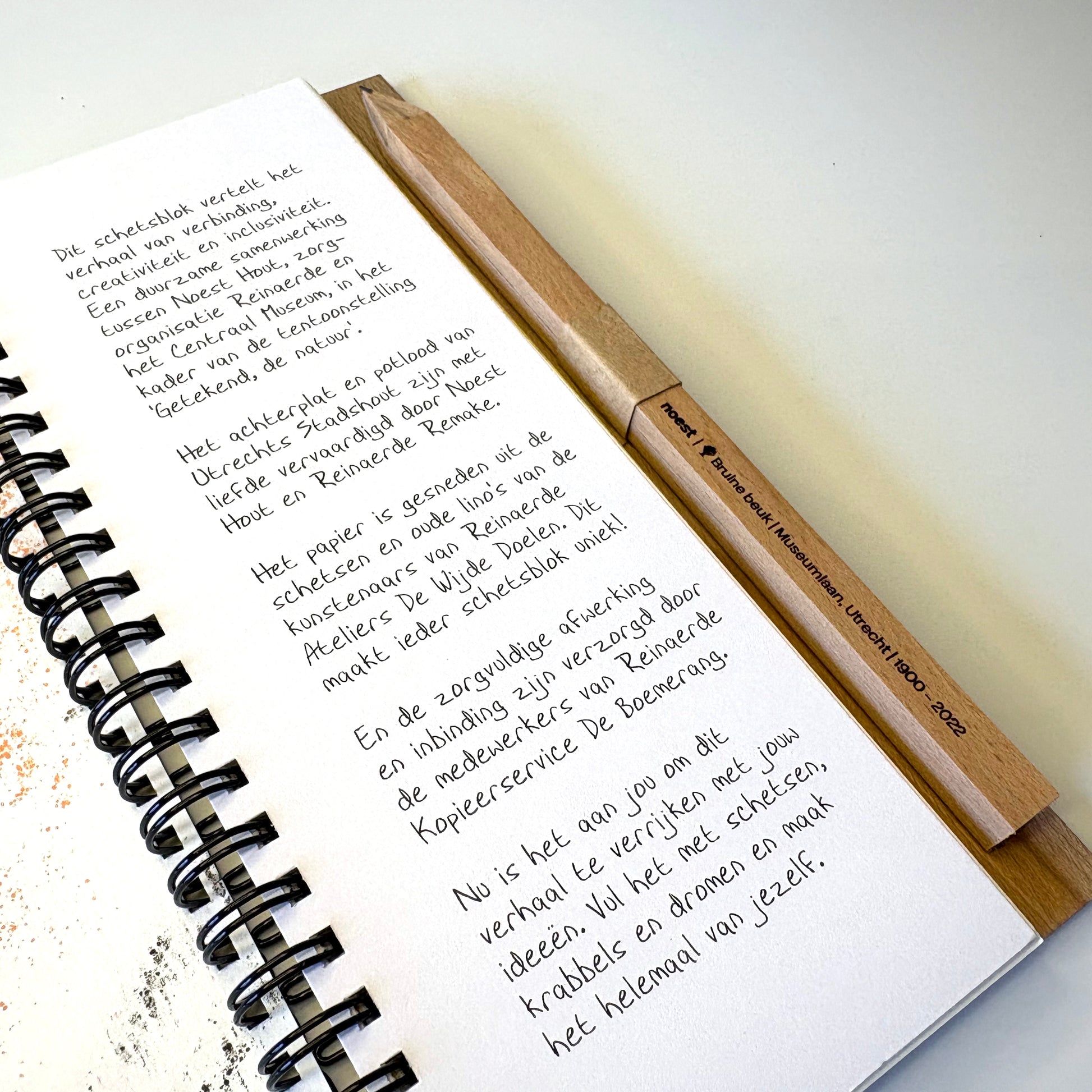 Het schetsblok opengeklapt op tafel, toont gerecycled papier en gepersonaliseerd potlood